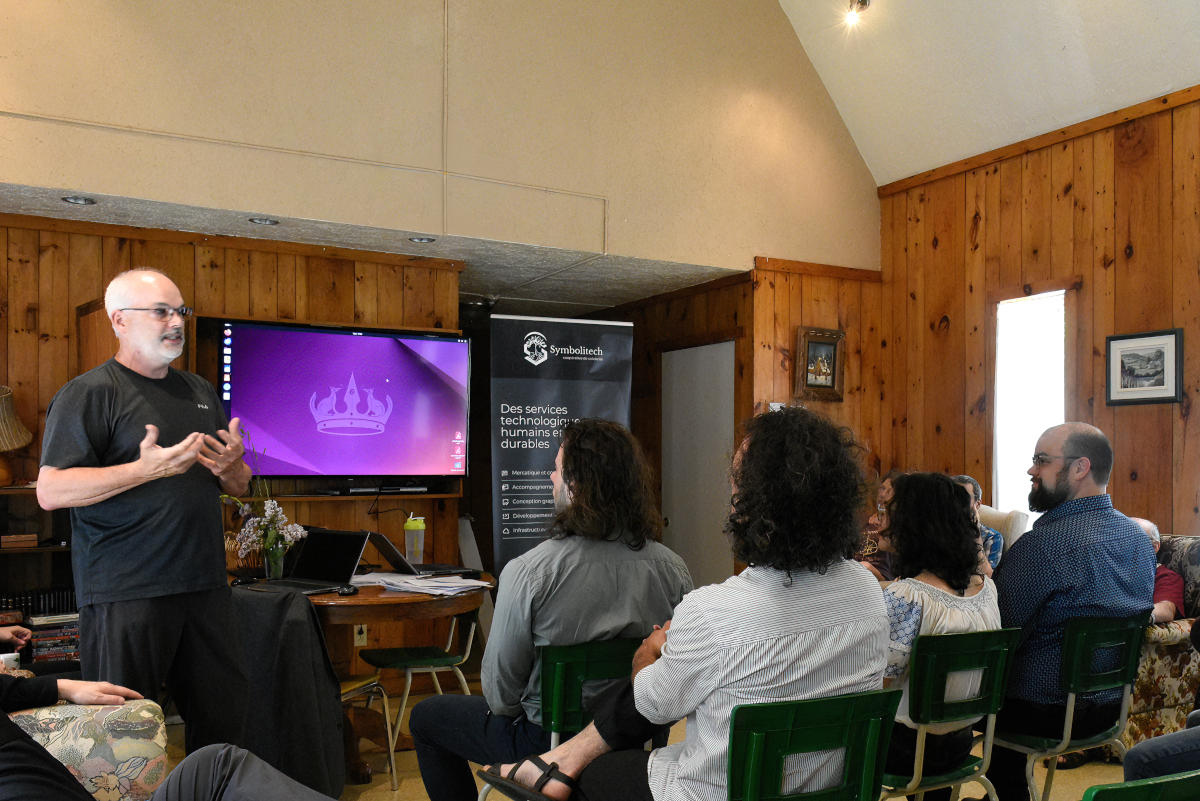 Photo d'une salle avec des membres de Symbolitech, un écran d'ordinateur Ubuntu et une bannière de la coopérative